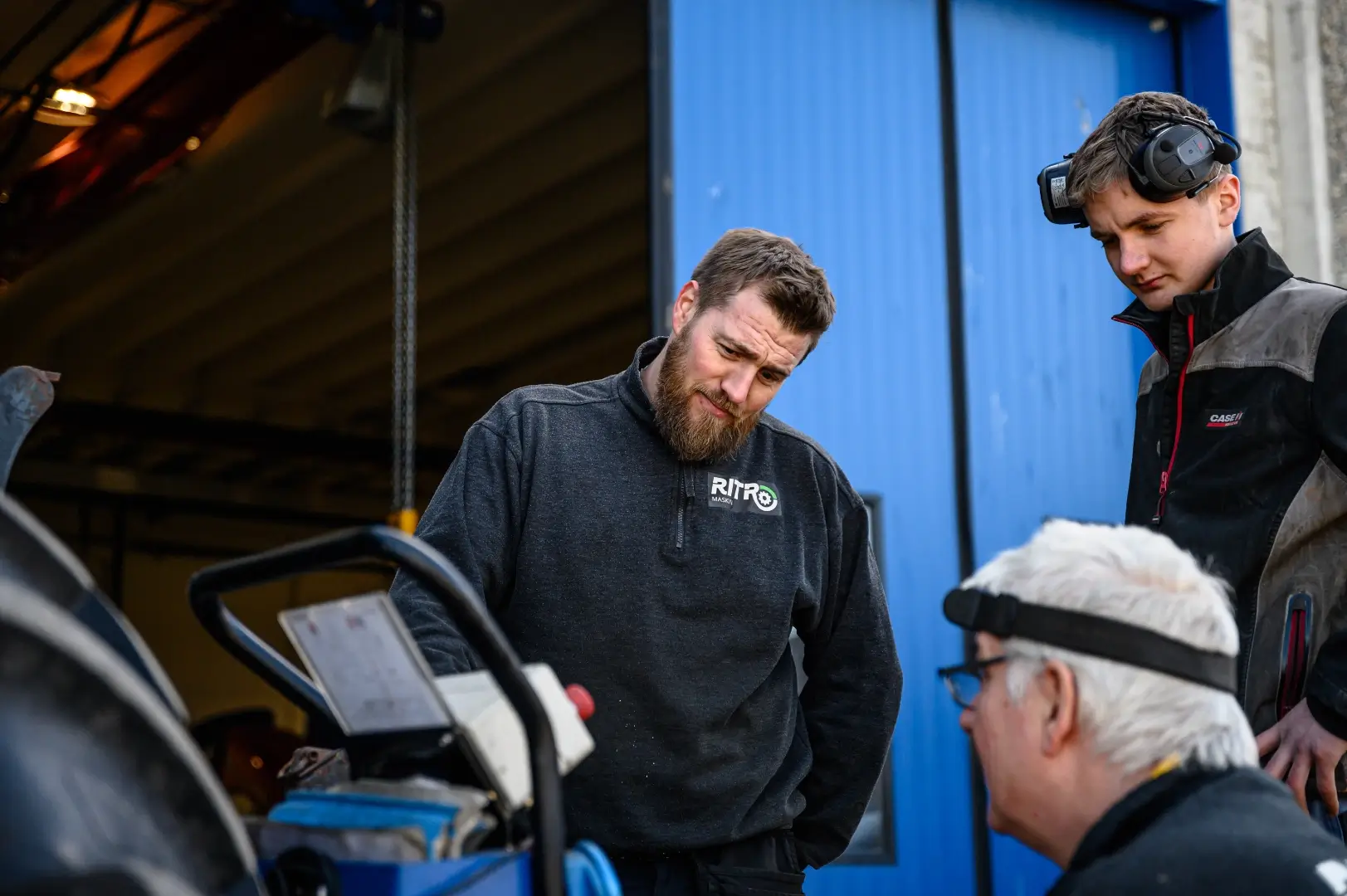 mekanikere står rundt en traktor og snakker sammen.