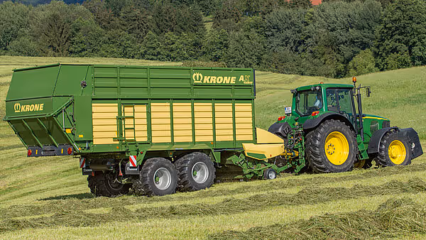 KRONE AX rotorballe trukket av grønn traktor som høster og hakker fôr inn i vogna på eng.
