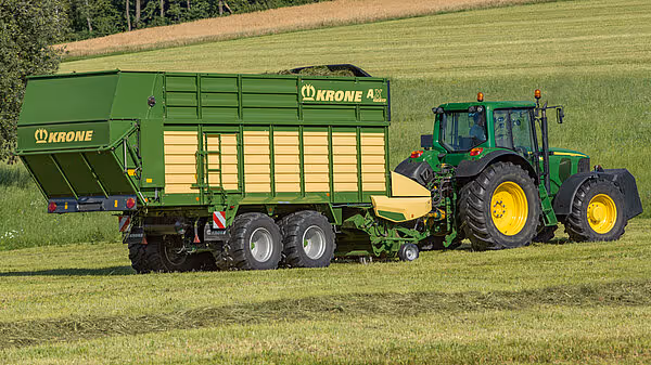 John Deere-traktor med grønn KRONE AX silotransportvogn i felt under høsting.