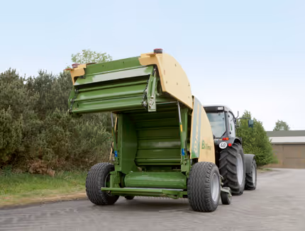 Krone Bellima rundballpresse i gul og grønn farge trukket av en traktor på en vei.