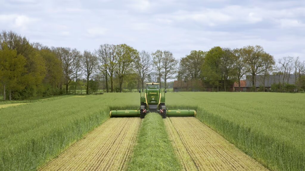 KRONE Big M 450 slåmaskin i arbeid på eng med tre meieskjermer utfoldet. Maskinen meier gress og etterlater seg ferdig slått areal.