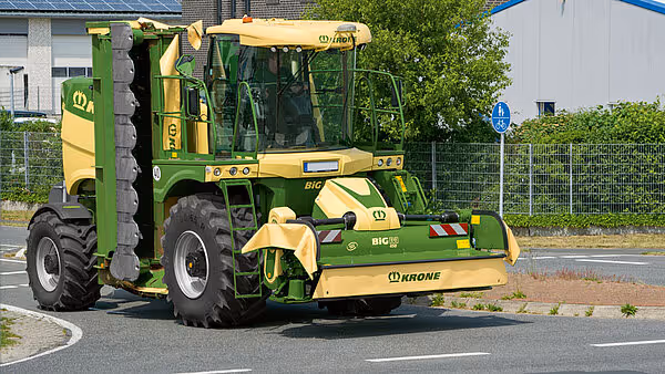 KRONE Big M 450 selvgående slåmaskin kjører på asfaltert vei gjennom boligområde.