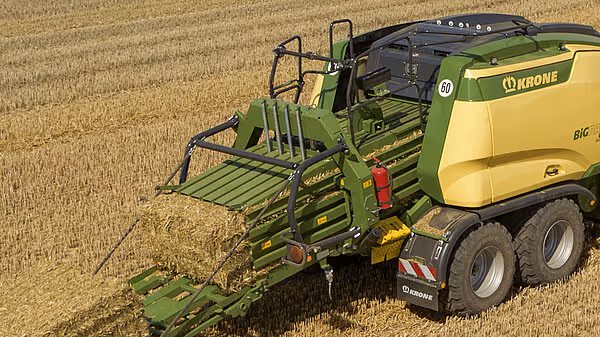 KRONE BigPack rundballpresse i arbeid på kornstubber, maskinens grønne og gule design er tydelig synlig. Pressa samler halm fra kornhøsting på åkeren.