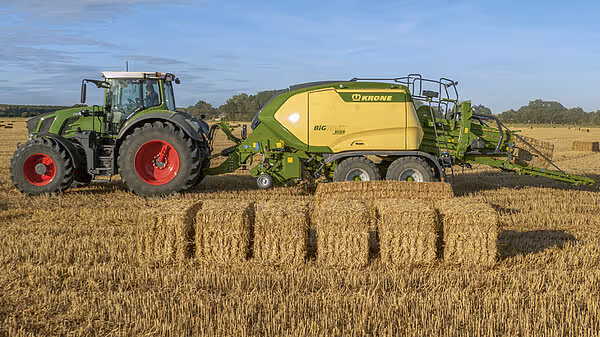 Fendt traktor trekker Krone BigPack storballepress på åker med ferdigpressede storballer i bakgrunnen.