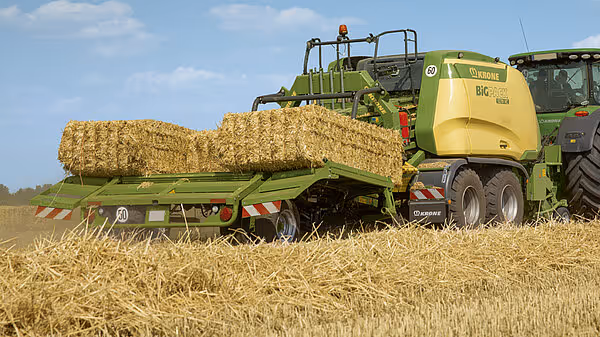 En Krone BigPack storballpresse produserer firkantede storballer i et stubbeåker, med en grønn traktor som driver maskinen.