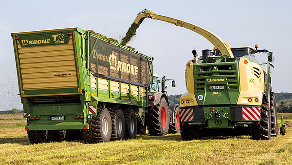 Krone Big X som fyller en Krone tilhenger under høsting på jordet.