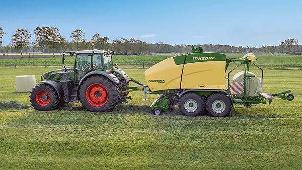 KRONE Comprima Plus rundballpresse arbeider på grønn eng eller beite. Maskinen pakker gras eller høy til rundballer under optimale arbeidsforhold.