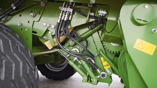 Underside av Krone Comprima Plus som viser hydrauliske komponenter og drivverk i grønt stål.