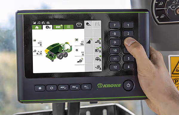Hånd som betjener en CCI kontrollterminal med berøringsskjerm som viser grønn traktor-ikon og numerisk tastatur til høyre.