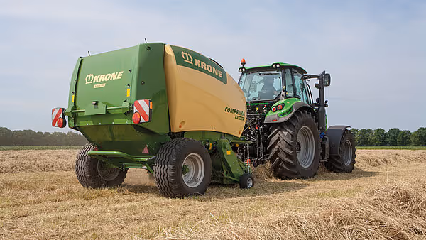 KRONE Comprima rundballpresse i arbeid på stubbeåker med traktor som trekkraft.