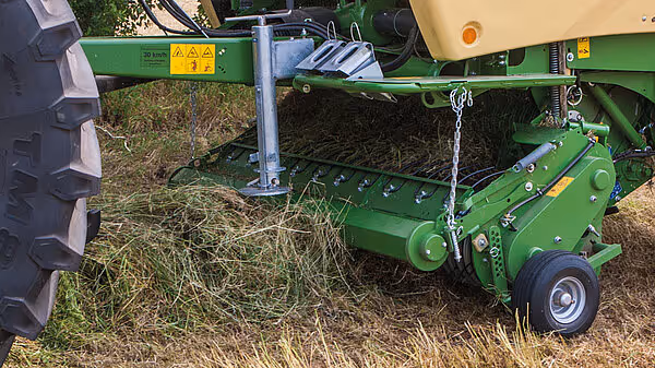 KRONE Comprima rundballpresse som samler høy fra bakken med oppsamlingsenheten. Maskinen er grønn og har store traktorhjul.