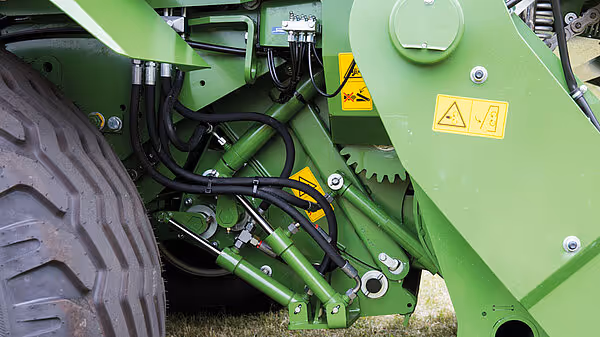 Hydraulisk system og kjedestrammer med advarselsskilt på Krone Comprima rundballpresse.