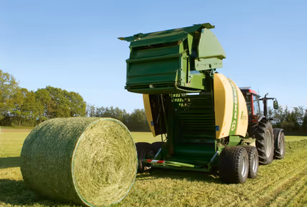 KRONE Fortima rundballpresse i drift på åker med ferdig rundballe ved siden av maskinen.