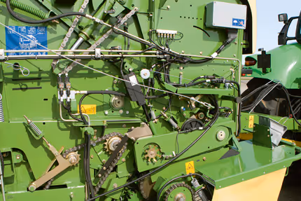 Detaljbilde av knivverket og mekaniske komponenter på en grønn KRONE Fortima rundballpresse. Komplekse hydrauliske slanger og drivverk er synlig.