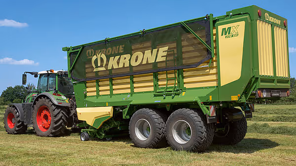 KRONE MX fôrvogn med to aksler trukket av Claas traktor på eng, viser siden av vognen med karakteristisk grønn og gul farge.