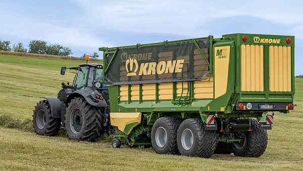 Sort traktor med påhengsvogn kjører på eng med Krone MX silofyll-vogn på slep.