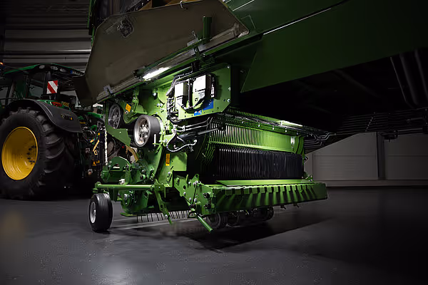 KRONE RX høstmaskin med grønn farge og gule felger, fotografert innendørs fra siden med tilhørende traktor.