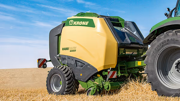 KRONE Varipack rundballpresse i gult og grønt arbeider på en stubbåker, trukket av en grønn traktor.