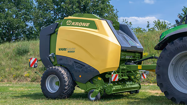 Krone Varipack Plus rundballer i arbeid på eng, tilkoblet grønn traktor.