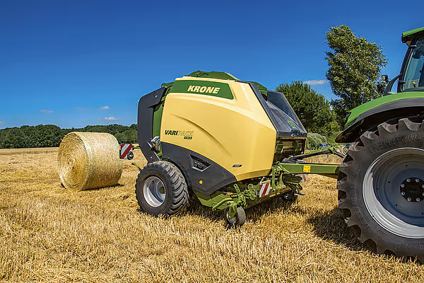 KRONE VariPack Pro rundballpresse i arbeid på stubbåker med traktor. Maskinen produserer store rundballer av halm under blå himmel.