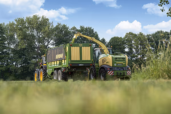 KRONE ZX silokjerre blir fylt fra en hakkemaskin på en grønn slåttopp i felt.